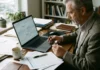 Investor ve home office analyzuje graf akcií Berkshire Hathaway na notebooku mezi papíry s finančními daty