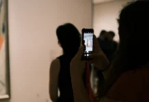 Žena si v galerii fotografuje abstraktní obraz mobilem a prohlíží si ho před nákupem