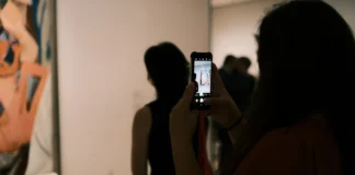 Žena si v galerii fotografuje abstraktní obraz mobilem a prohlíží si ho před nákupem