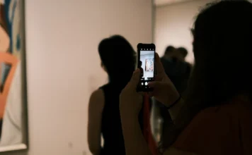 Investice do umění: jak začít a na co si dát pozor Žena si v galerii fotografuje abstraktní obraz mobilem a prohlíží si ho před nákupem