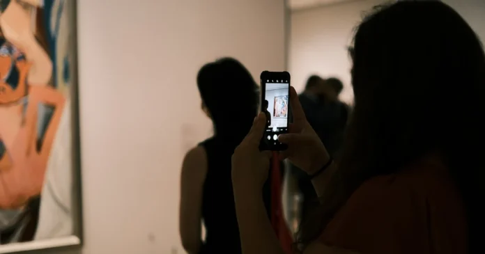 Žena si v galerii fotografuje abstraktní obraz mobilem a prohlíží si ho před nákupem